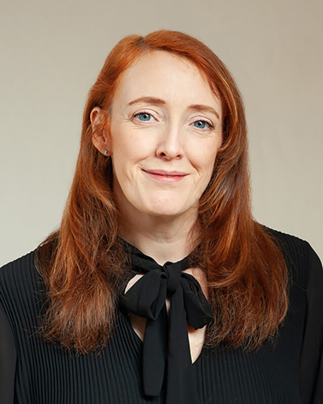 Headshot of red haired business woman in black top against a light background