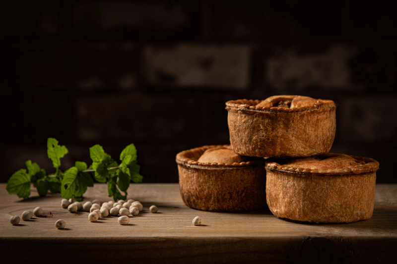 Three Pork pies with uncooked peas and garnish sitting on a wooden board
